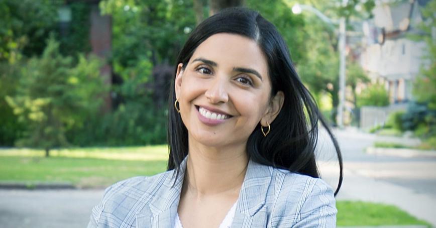 Dr. Sonia Kang in a grey blazer in front of green trees on a campus.