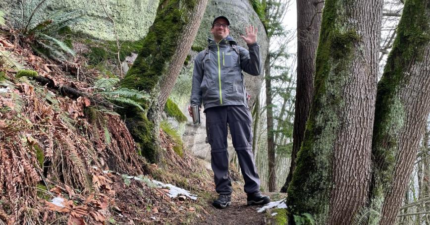 Rob Newell standing in a forested area waving at the camera