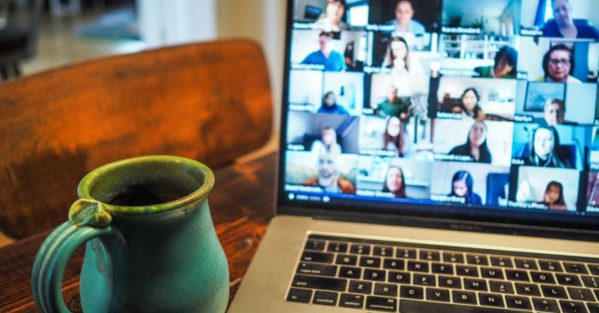 A laptop displaying a video call next to a mug on a table.