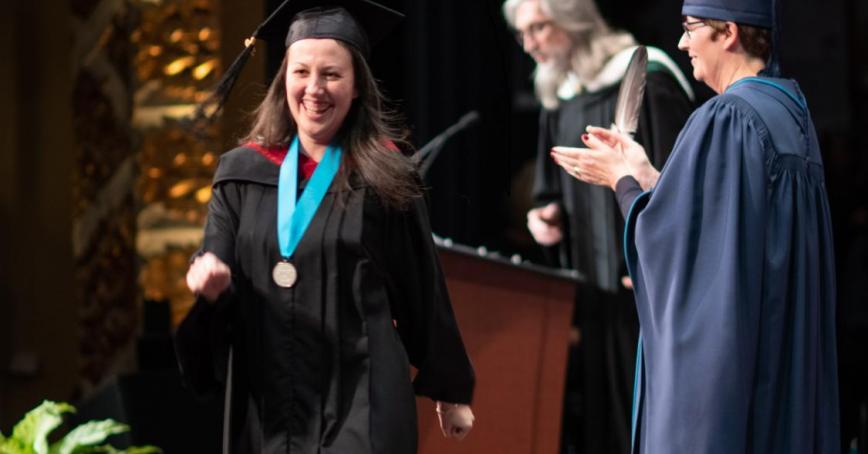 A happy graduate from a past Convocation strolls across stage with her academic medal.