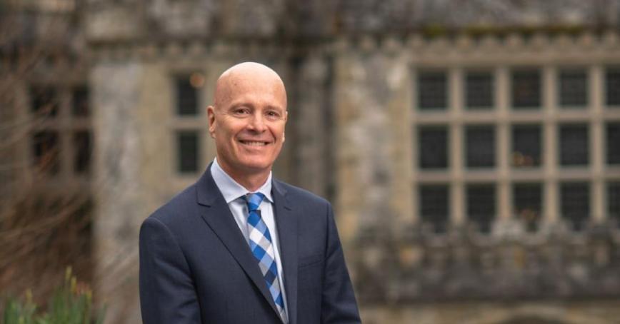 Smiling man in dark suit in front of grand old stone building