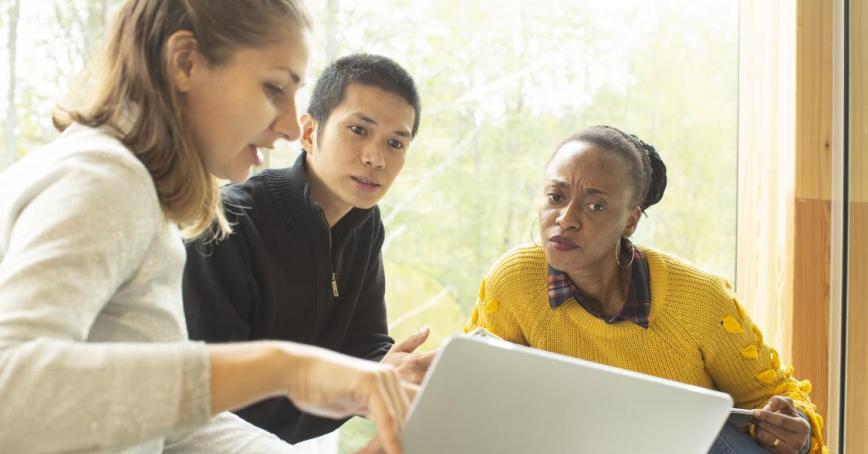 3 people sitting around a laptop