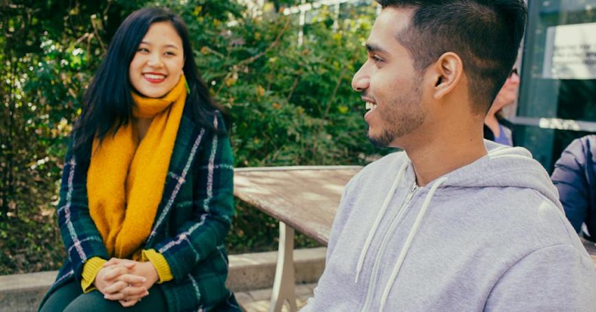 Two individuals sitting on a bench outside and smiling