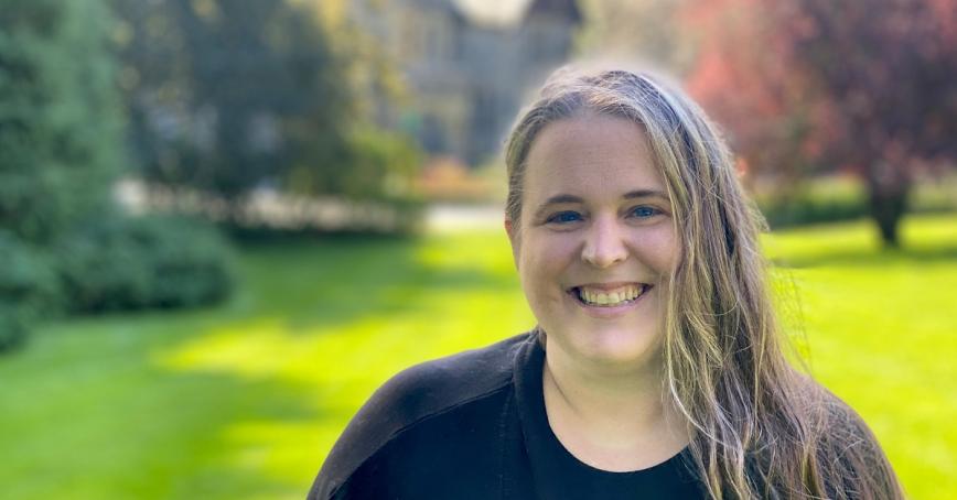A smiling Alli Boyd stands in the foreground with the castle and green lawn blurry in the background. She looks delighted.