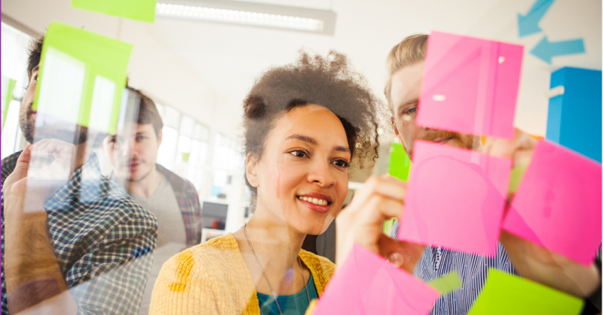 A group of people brainstorm on colourful post-it notes on a window.