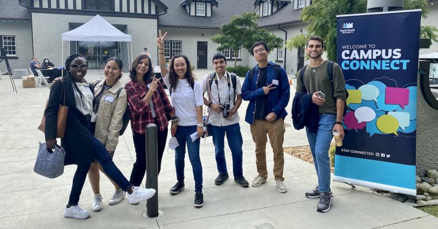 A group of students outside the Sherman Jen Building pose in front of a Campus Connect banner.