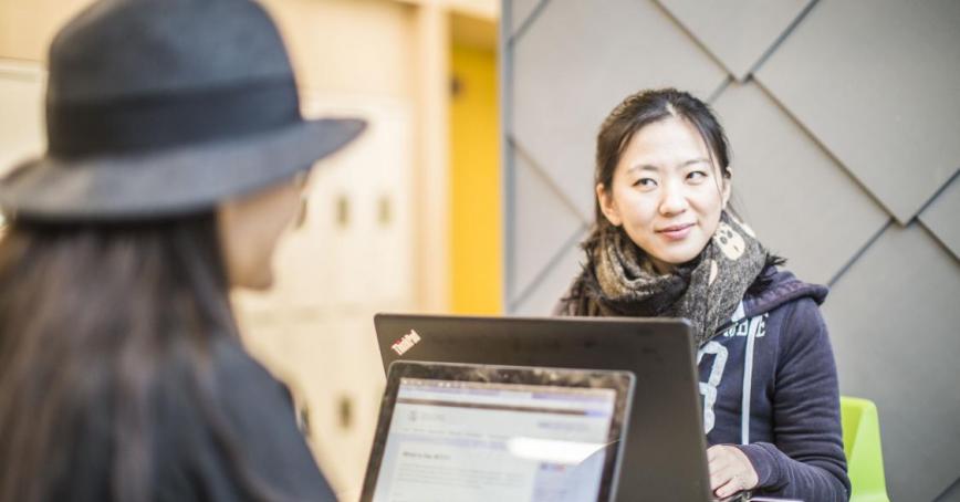 two people sitting at a table working on their laptops