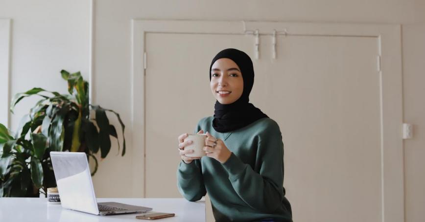 A female in a hijab sitting on a chair with a mug in her hands