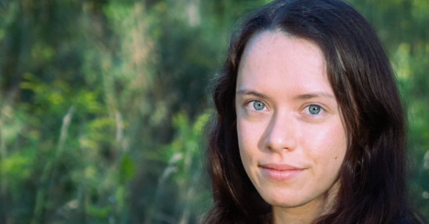 A head shot of a woman with greenery in the background.