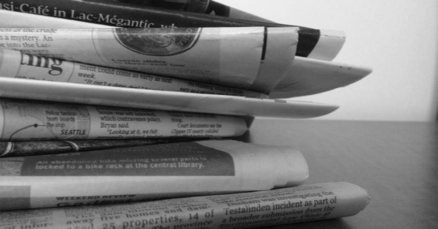 Pile of newspapers on a desk.