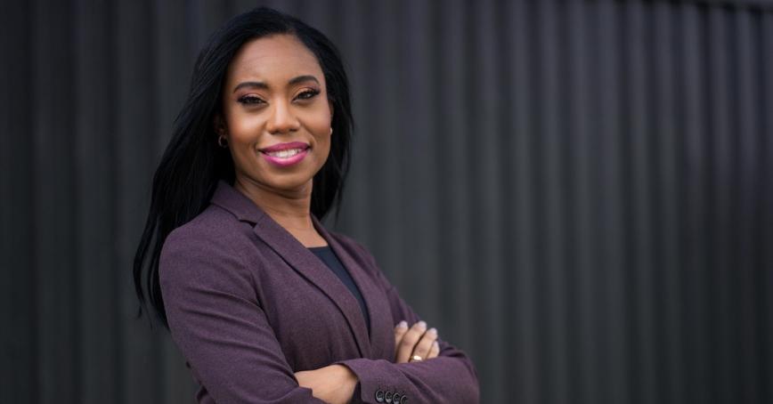 RRU grad Siobhan Calderbank, a Black woman in a purple suit jacket, crosses her arms and smiles.
