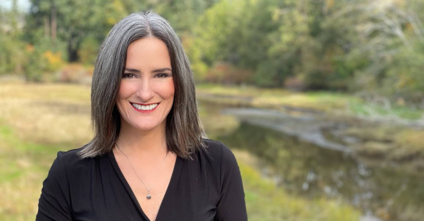 Head shot of Jill McAbe stanind in front of a grassy field surrounded by trees