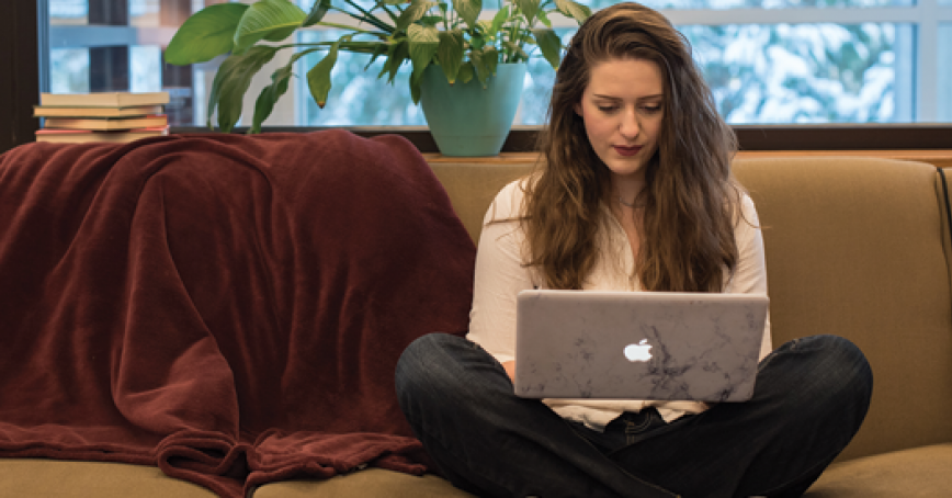 A student on a couch looking at the laptop