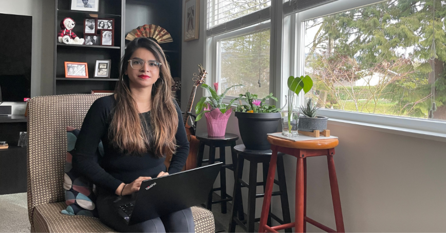 Eshwari Murumkar sitting on a chair with a computer on her lap, next to a large window to the right