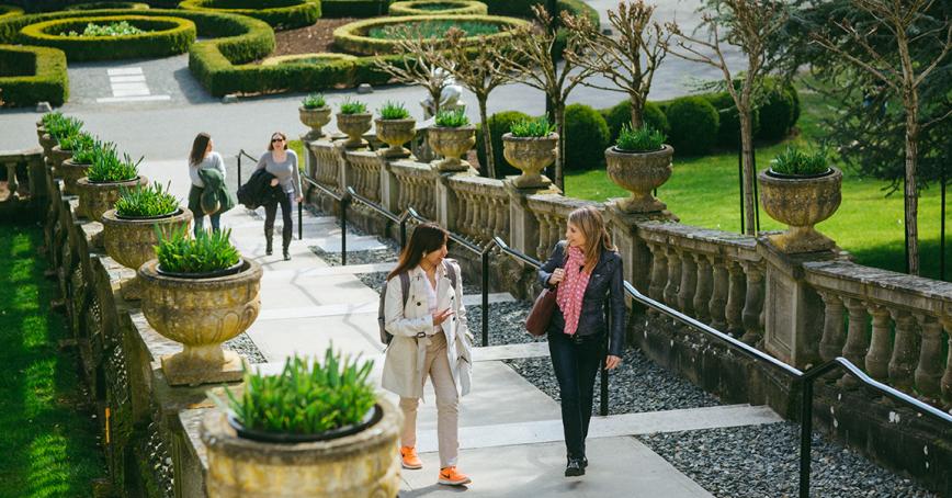 Two pairs of students walk up the flat, wide concrete steps of the Neptune Staircase on campus. Manicured hedges can be seen in the background.