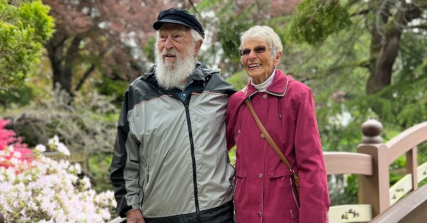Dick (left) and Bette (right) Geisreiter standing arm in arm on a bridge in the Royal Roads Japanese Garden.