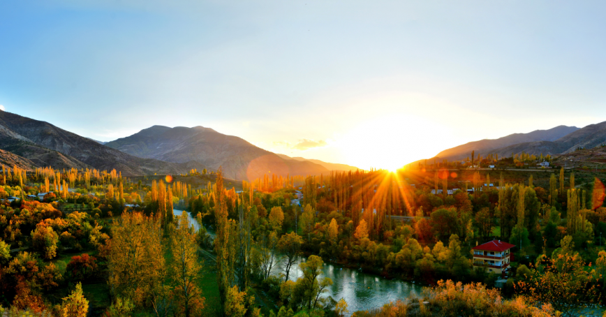 A setting sun peeks out from behind a forested mountain range.