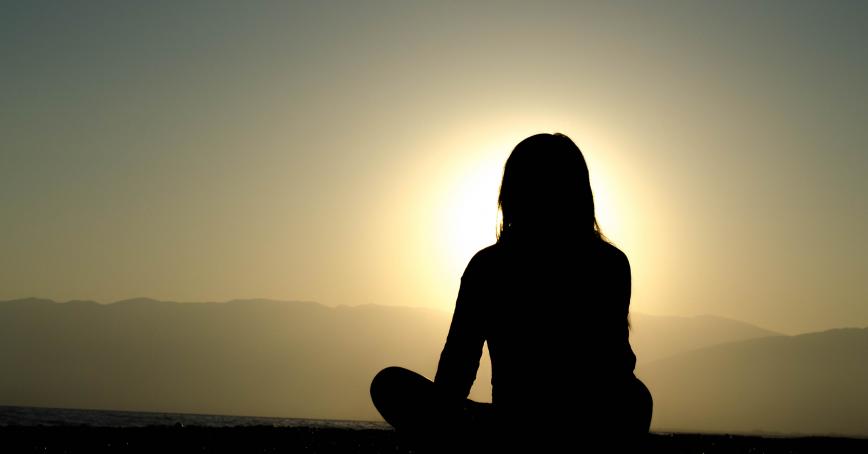 shadow of a person sitting in front of a rising sun