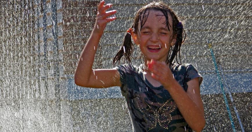 A child plays under an outdoor sprinkler 