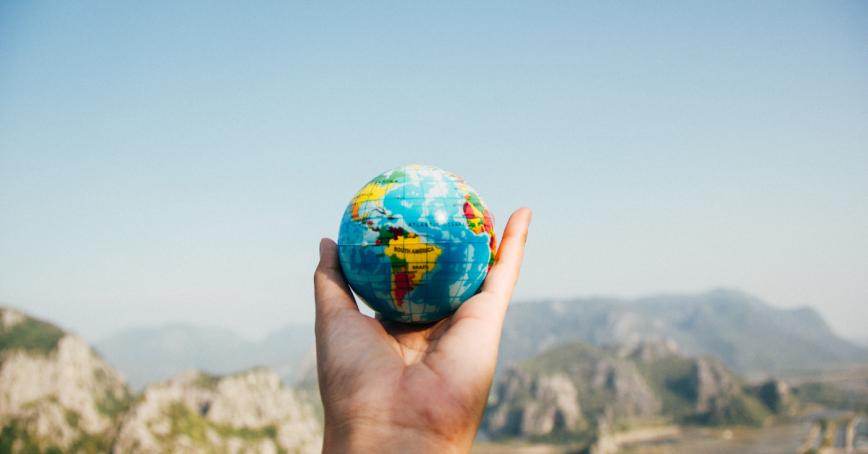 An outstretched hand holds a globe. Mountains can be seen in a distant background.