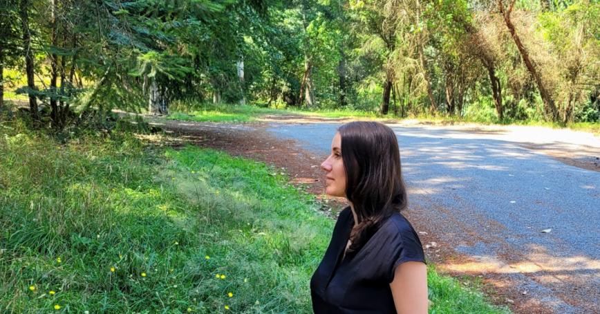 A woman stands near the forest looking into the distance