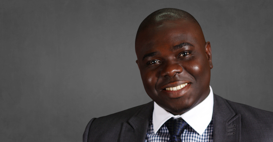 A headshot of Tade Owodunni wearing a suit and tie.