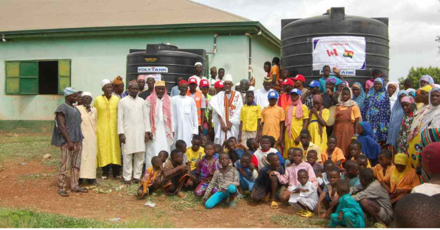 A large group of people pose in front of a water collection tank in Ghana.