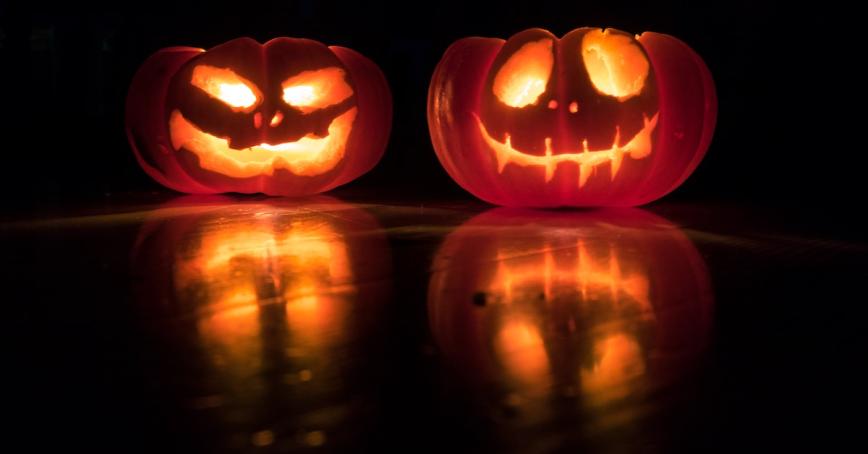Two jack o lanterns with a dark background. Their reflections are visible at the front.