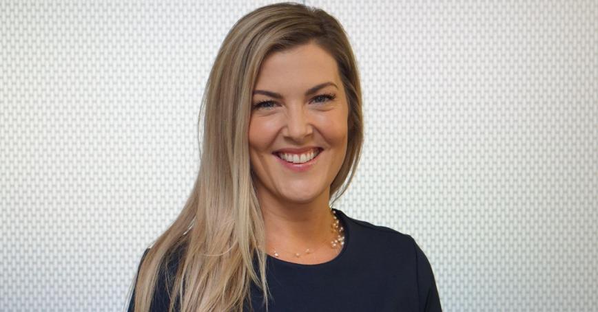 Tess York, wearing a navy blue shirt standing in front of a grey background