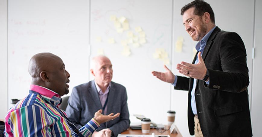 Two DBA students sitting at a table discussing their work with Dr. Hassan Wafai, DBA program head.