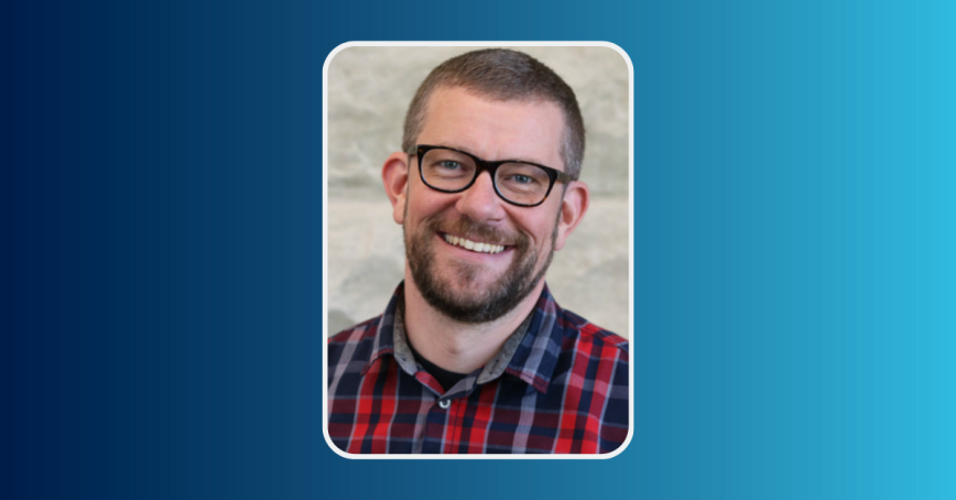 A headshot of a smiling Chris Campbell in a plaid shirt and glasses.