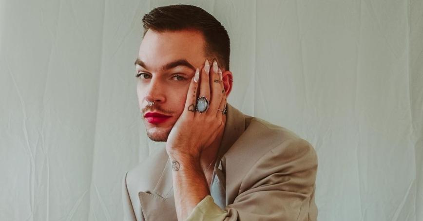 Jan Van Vianen poses in front of a white background with his head in his hand which has white stiletto-style fingernails and rings