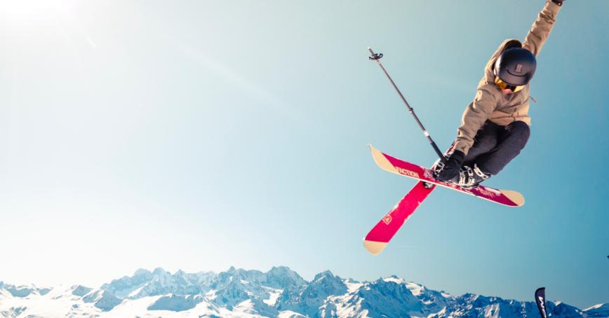 Person mid jump while skiing. Blue mountains in the background with the sun shining.