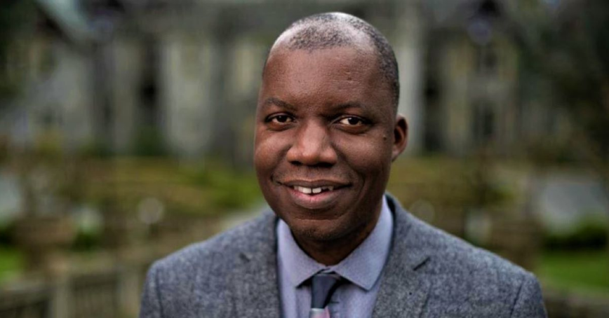 Nathan Banda stands in front of Hatley Castle, wearing a grey suit and tie