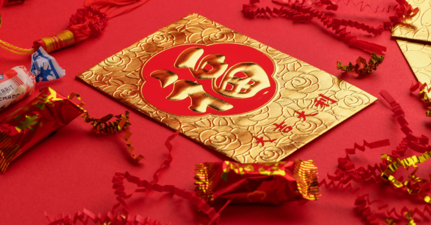 A table with a red table cloth with candy and a golden envelope on it. 