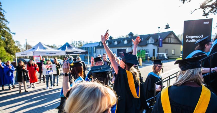 Graduates of Royal Roads University celebrate in a large group outside the Dogwood Auditorium