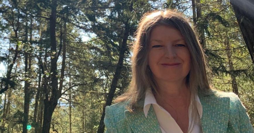 Woman in green suit jacket smiling with the sun shining behind her