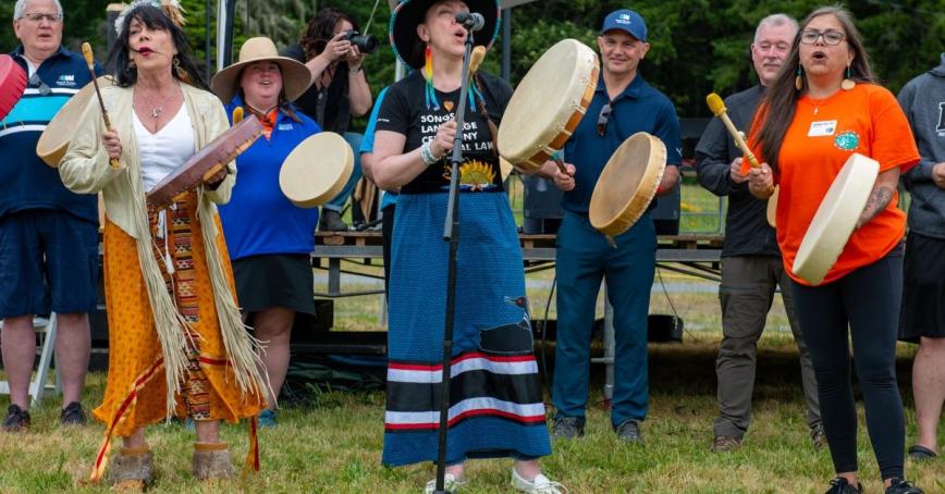 A group of people with drums sing near a microphone