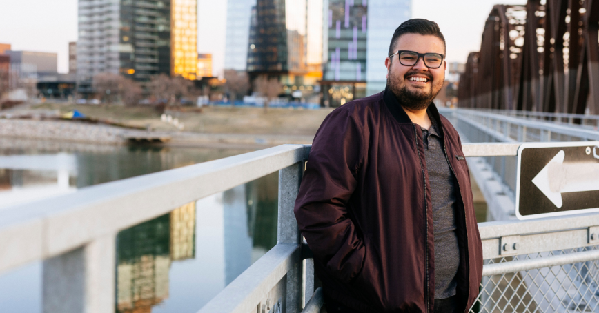 A man stands and poses for a picture against a cityscape.