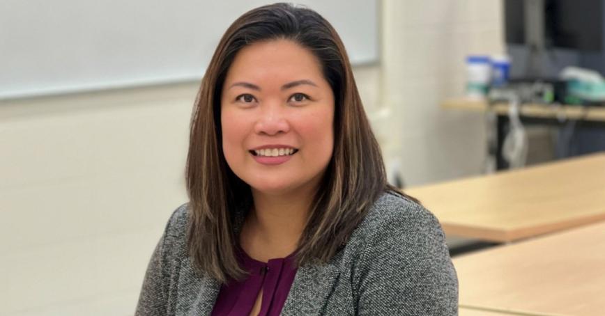 Woman smiling directly at camera with a whiteboard behind her.