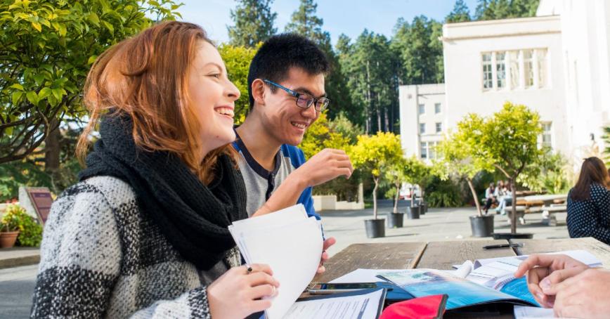 International students sit outside at Royal Roads University, conversing around a picnic table.
