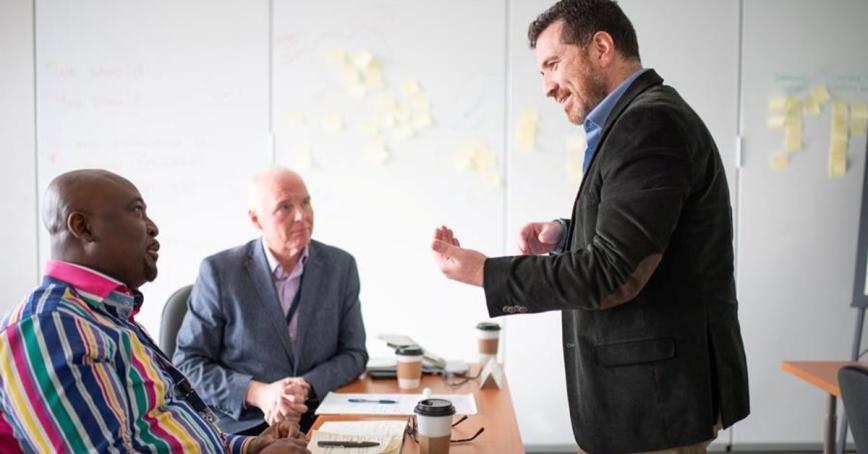 An instructor stands in front of two students who are seated directly in front during a classroom lecture