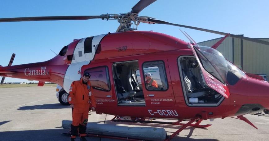 Man standing in front of red helicopter on tarmac.