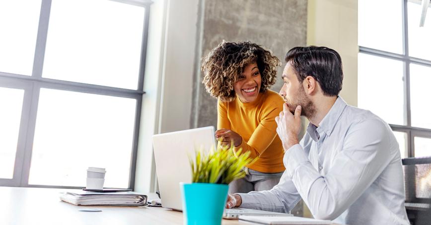 Two people side-by-side, smiling at a laptop indoors.