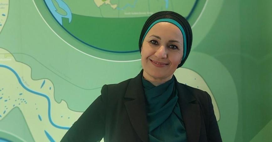 Wasan Jema, wearing a black head covering, stands in front a wavy green backdrop.