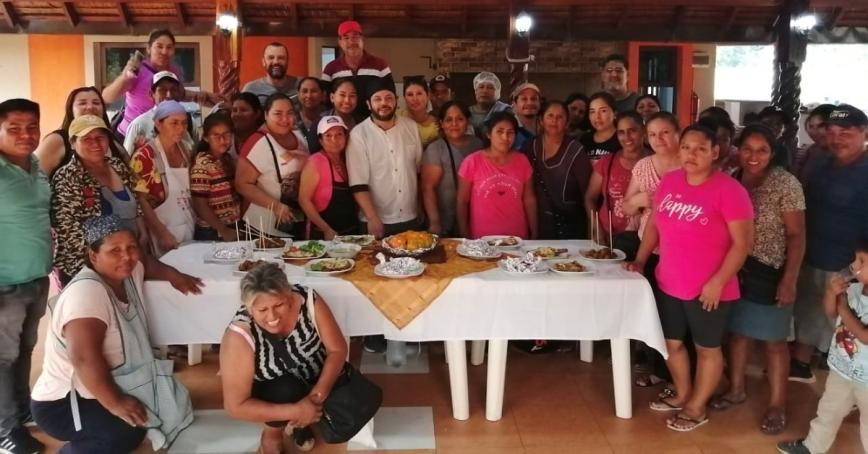 Large group of people standing around a table filled with various food dishes.