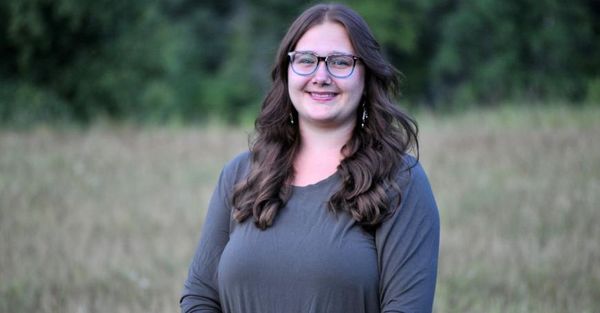 Leeza Perehudoff smiling at camera with a field of grass behind her. 