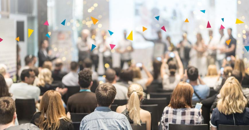 An audience of people seated in an auditorium look on toward a stage of award winners