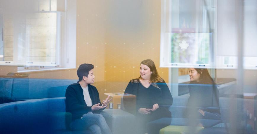 A group of RRU students sit outside a classroom on a blue couch in conversation.