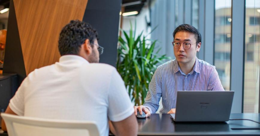 Taejo Kim sits across the desk from a student, in an office environment
